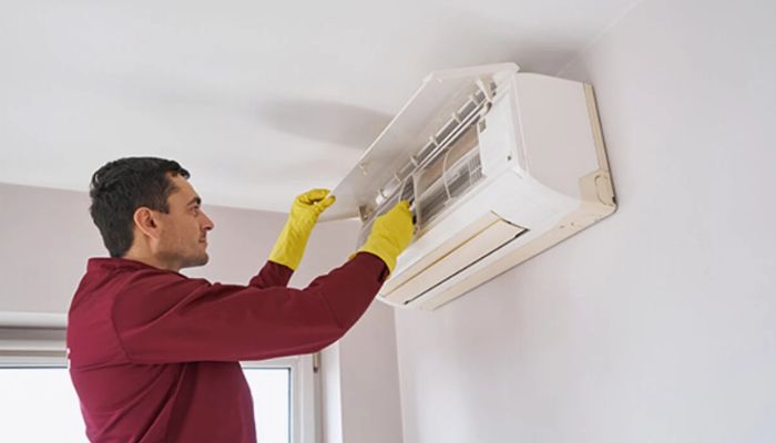 Foto de um homem de luvas fazendo a manutenção de um ar-condicionado