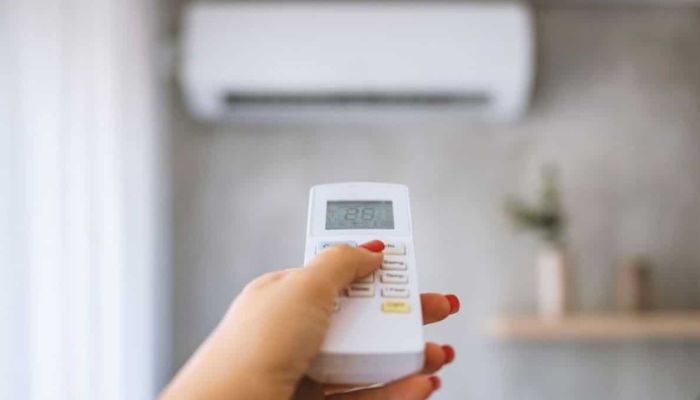 Foto de um ar-condicionado branco com uma pessoa apontando um controle remoto