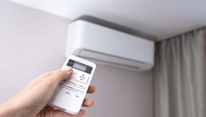 Foto de um ar-condicionado branca com uma pessoa apontando um controle